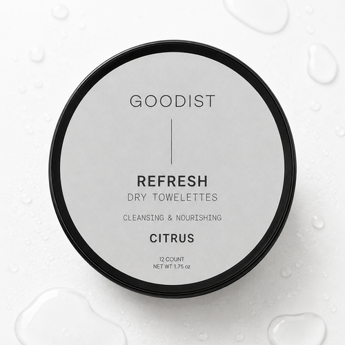 A round black lidded jar of Goodist Refresh Dry Towelettes in Citrus, photographed from above on a white surface with water droplets around it.