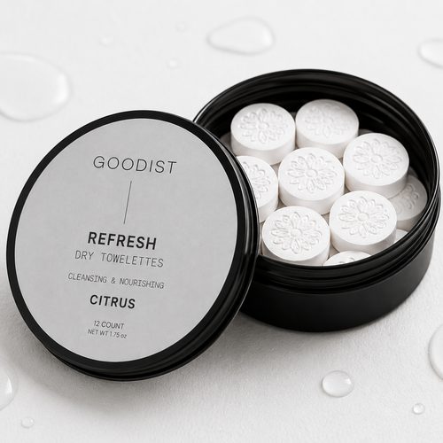 Goodist Refresh Dry Towelettes in a black round tin with the lid off, showing white circular towelettes inside, set on a white surface with water droplets.